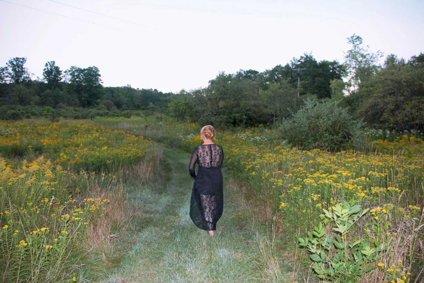 A performer walking through a field of goldenrod toward trees in the Catskills